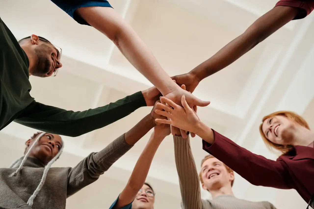 Home A diverse group of young adults forming a united circle with hands together indoors.