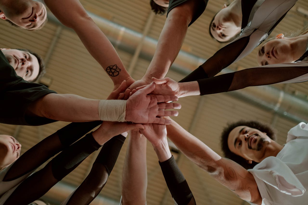Home A diverse group of people joins hands in a supportive team gesture from a low angle.